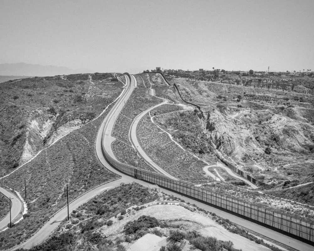 Une route sinueuse traverse un paysage désertique avec des collines, et une clôture longe la route.