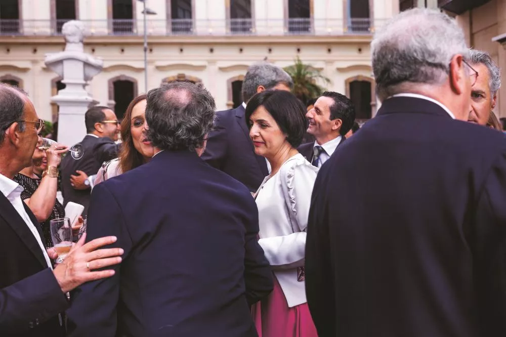 Un groupe de personnes bien habillées discute lors d'un événement en extérieur, devant un bâtiment historique. Certaines tiennent des verres à la main.