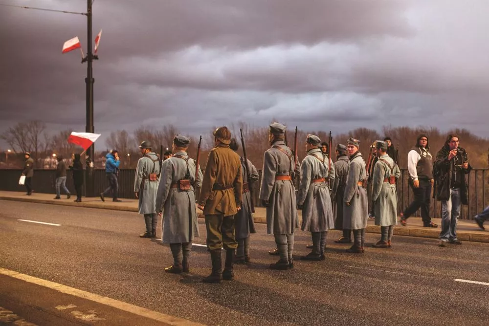 Un groupe de soldats en uniforme historique est aligné sur une route, avec un ciel nuageux en arrière-plan.