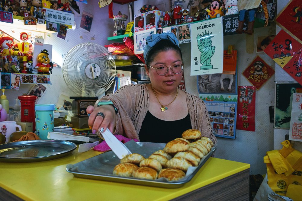 Une femme sert des pâtisseries sur un plateau dans un espace décoré de divers objets et affiches colorées.