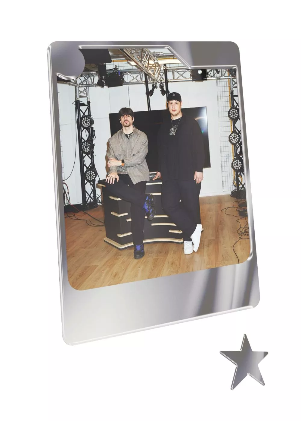 Deux personnes posent dans un studio avec des équipements d'éclairage en arrière-plan. L'une est assise sur un bureau, l'autre debout à côté.