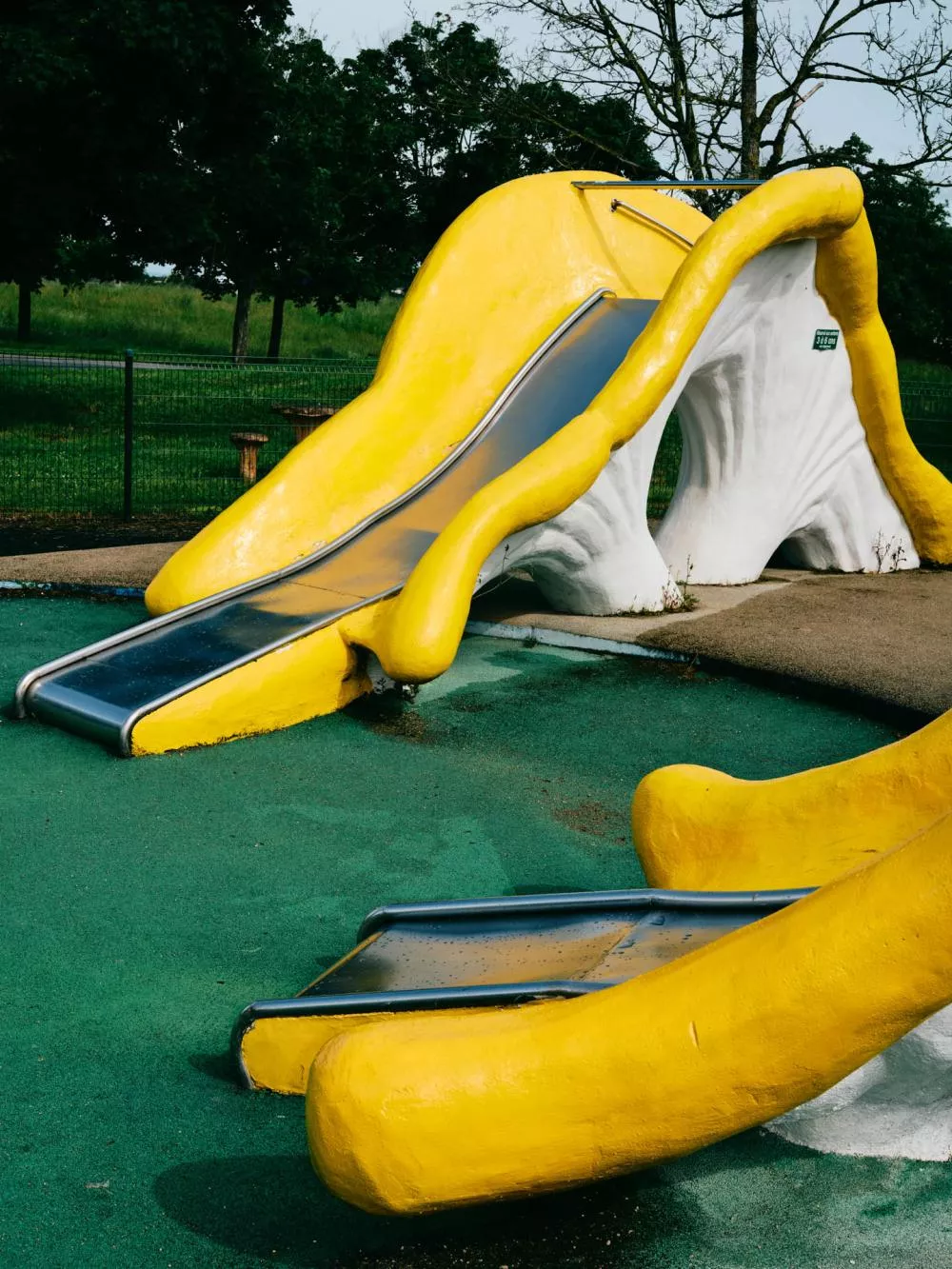 Un toboggan jaune et blanc dans une aire de jeux, avec un sol en caoutchouc vert.