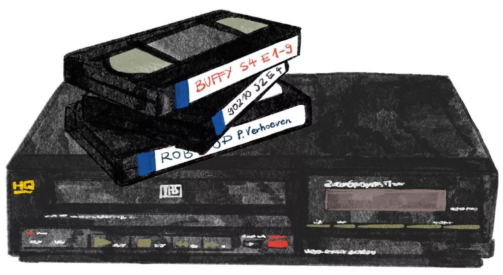 Un magnétoscope VHS avec trois cassettes empilées dessus, étiquetées "BUFFY S4 E1-9", "90210 S2 E4" et "ROBOCOP P. Verhoeven".