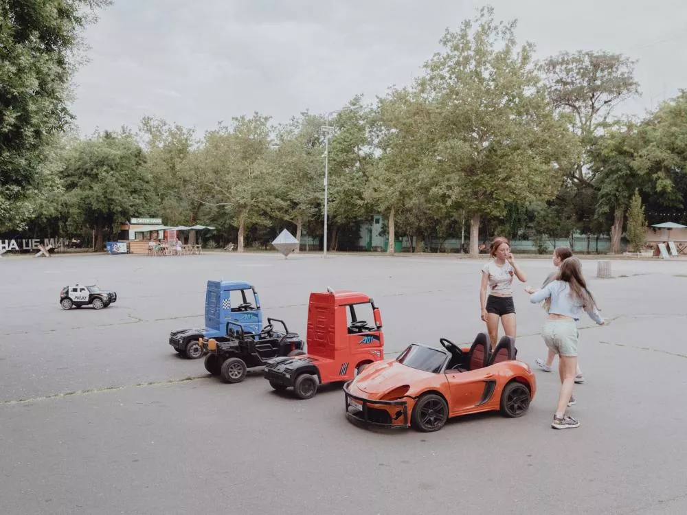Un groupe de jeunes filles joue autour de petites voitures électriques dans un espace ouvert entouré d'arbres.
