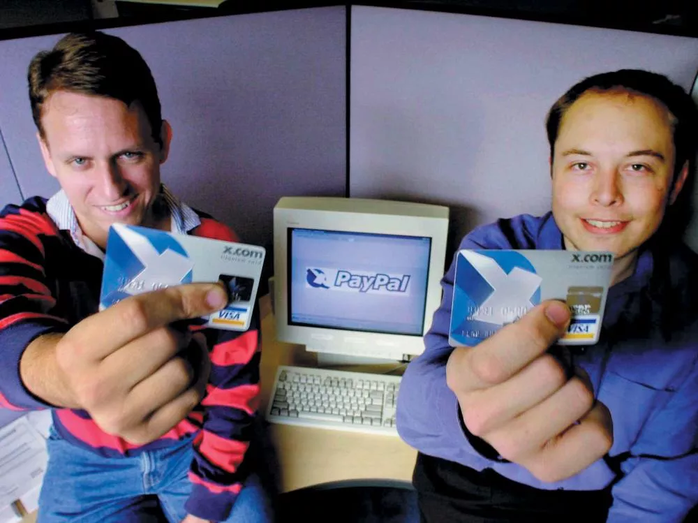 Deux personnes tiennent des cartes devant un ordinateur affichant le logo de PayPal.