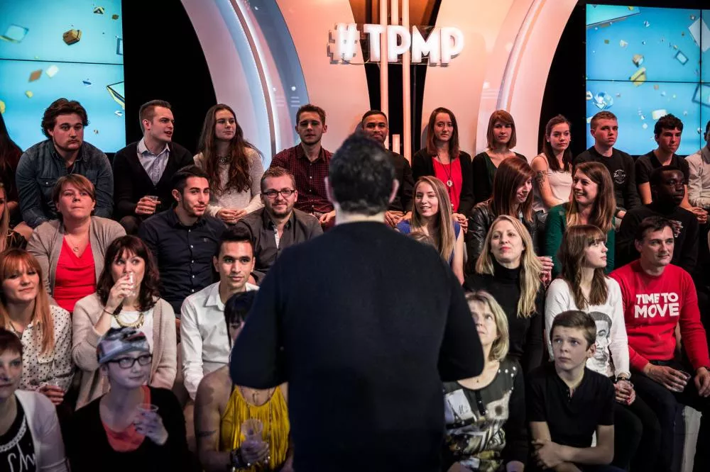 Un groupe de personnes est assis dans un studio de télévision avec le logo "#TPMP" visible à l'arrière-plan.