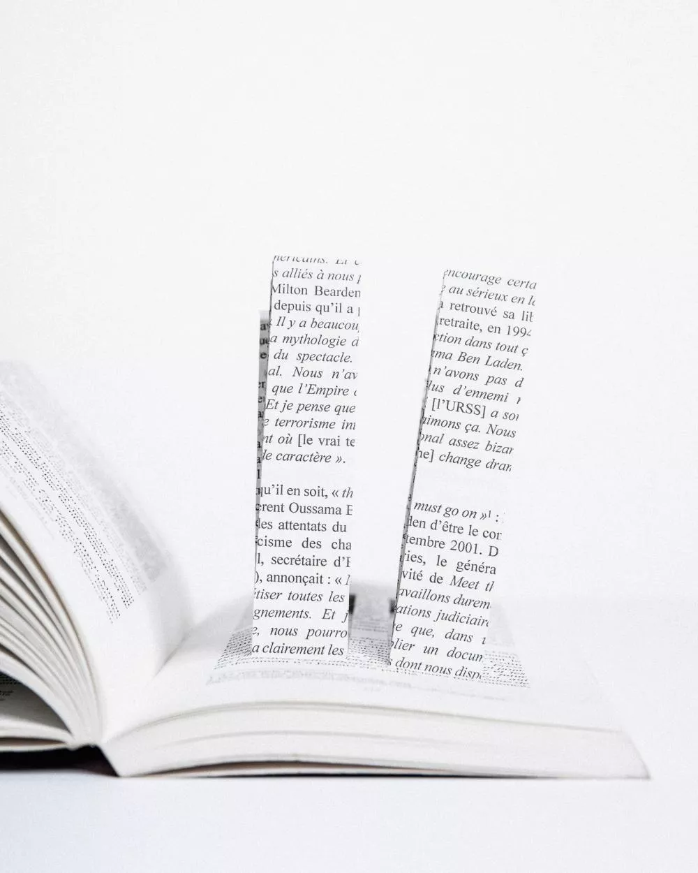Un livre ouvert avec deux morceaux de papier découpés en forme de lettres ou de chiffres, émergeant de ses pages, créant un effet visuel en trois dimensions.