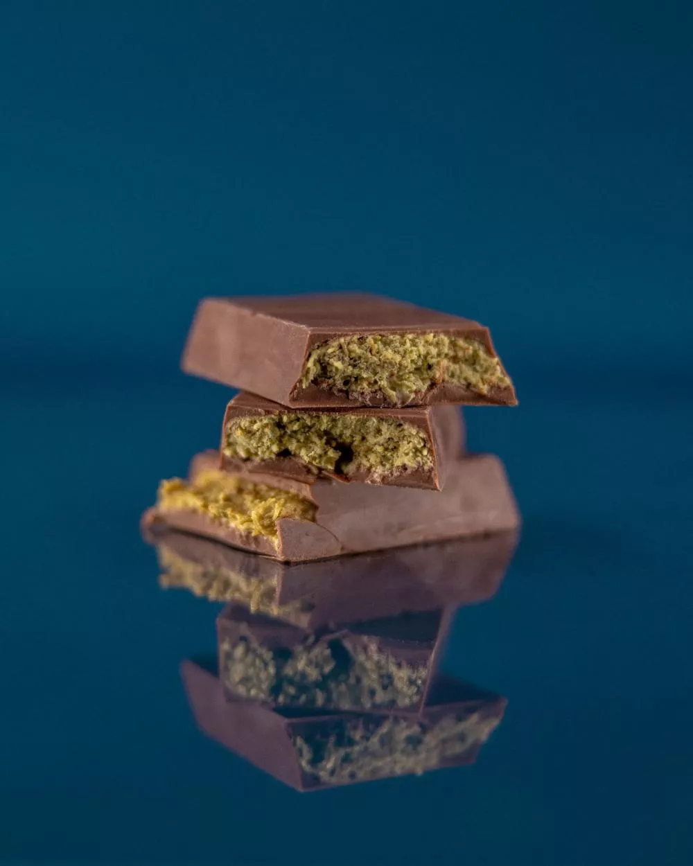 Des morceaux de chocolat empilés, avec une garniture verte visible à l'intérieur, sont posés sur une surface réfléchissante bleue.