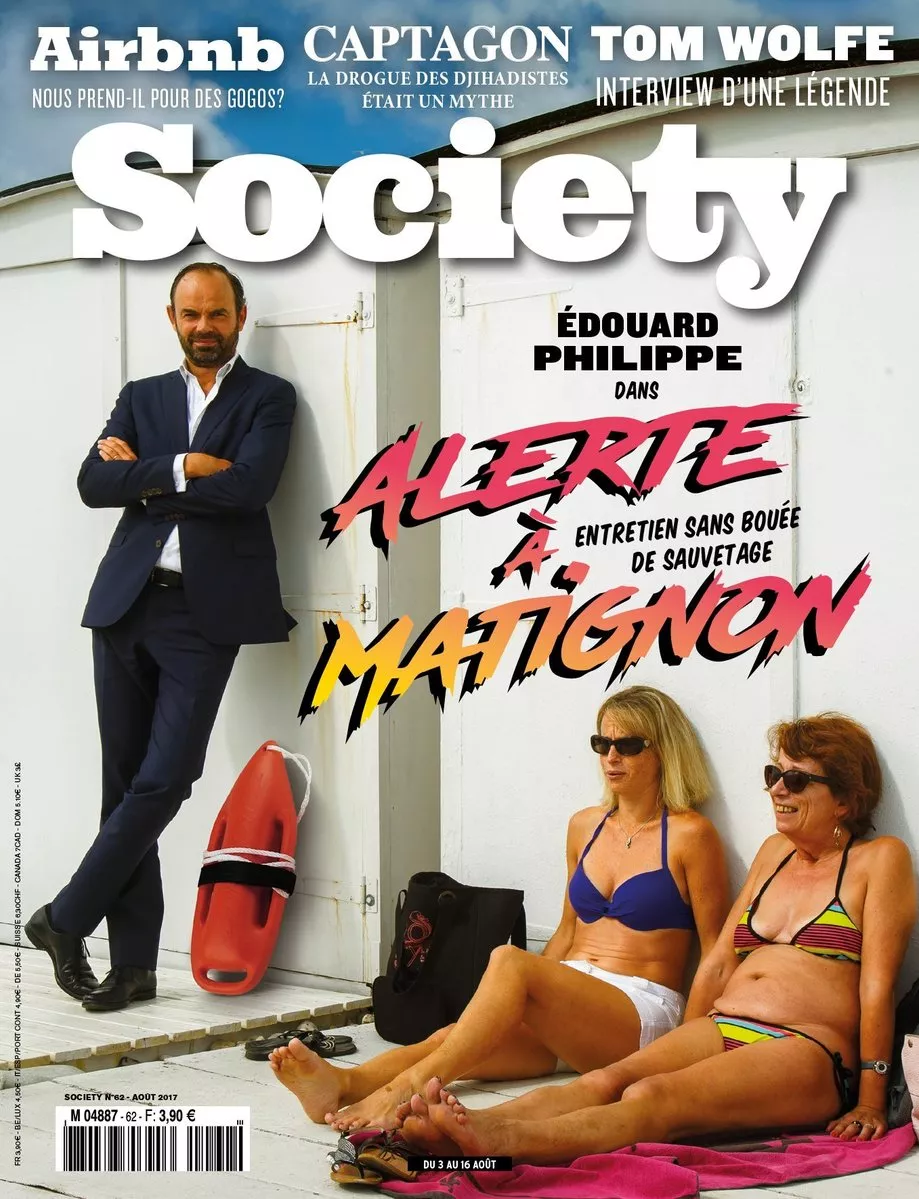 Un homme en costume se tient debout à côté d'une bouée de sauvetage rouge, tandis que deux femmes en maillot de bain sont assises par terre, adossées à un mur blanc. Le magazine "Society" mentionne un entretien avec Édouard Philippe intitulé "Alerte à Matignon".
