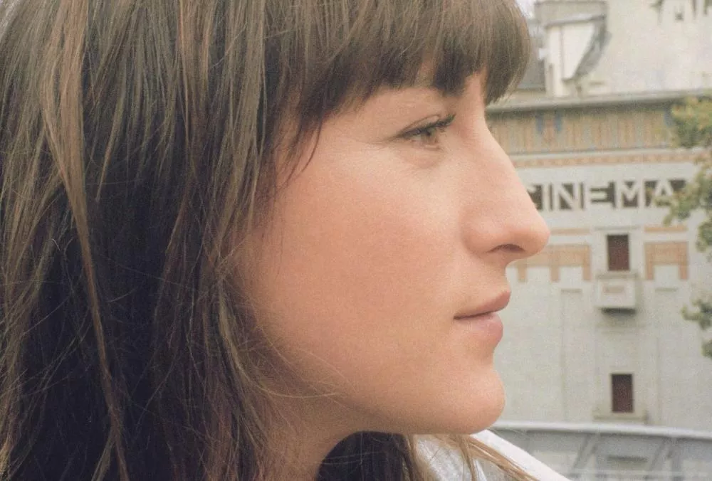Une femme de profil avec des cheveux bruns, en arrière-plan un bâtiment avec l'inscription "CINEMA".