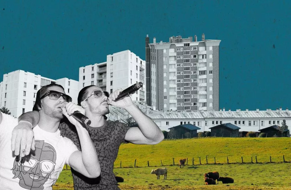 Deux personnes avec des micros chantent devant un montage d'immeubles résidentiels et un champ avec des vaches.