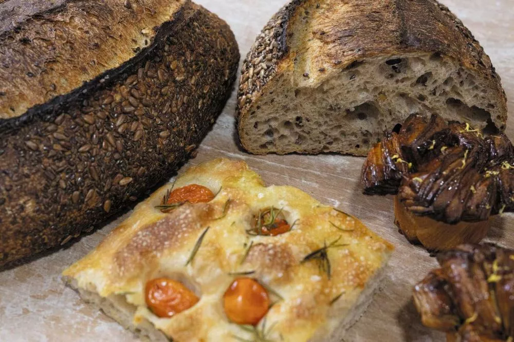 Un assortiment de produits de boulangerie comprenant un pain aux graines, une focaccia avec des tomates cerises et du romarin, et des pâtisseries feuilletées.
