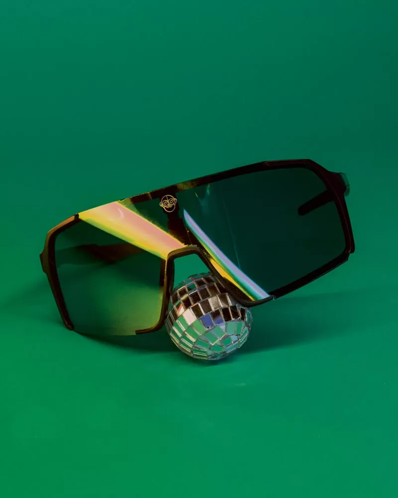 Des lunettes de soleil aux verres réfléchissants sont posées sur une petite boule à facettes, le tout sur un fond vert.