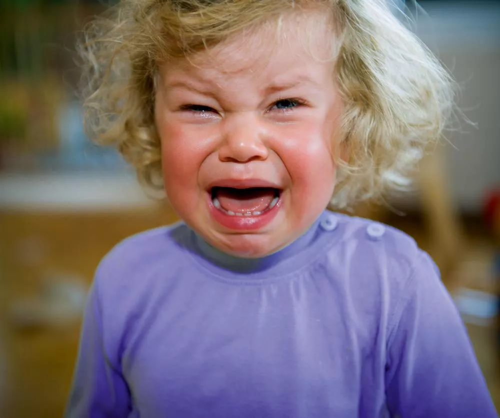 Un enfant en bas âge pleure, avec une expression de tristesse. Il porte un haut violet.