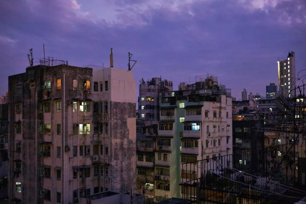 Une vue de bâtiments urbains au crépuscule, avec des lumières allumées dans certains appartements et un ciel violet en arrière-plan.