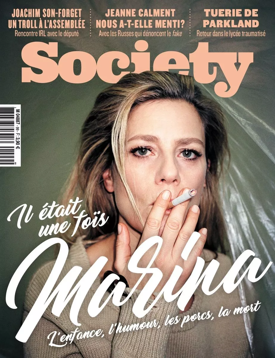 C'est la couverture du magazine "Society" avec une femme tenant une cigarette. Les titres incluent des sujets sur Joachim Son-Forget, Jeanne Calment, et la tuerie de Parkland. Le titre principal est "Il était une fois Marina" avec des sous-titres sur l'enfance, l'humour, les porcs et la mort.