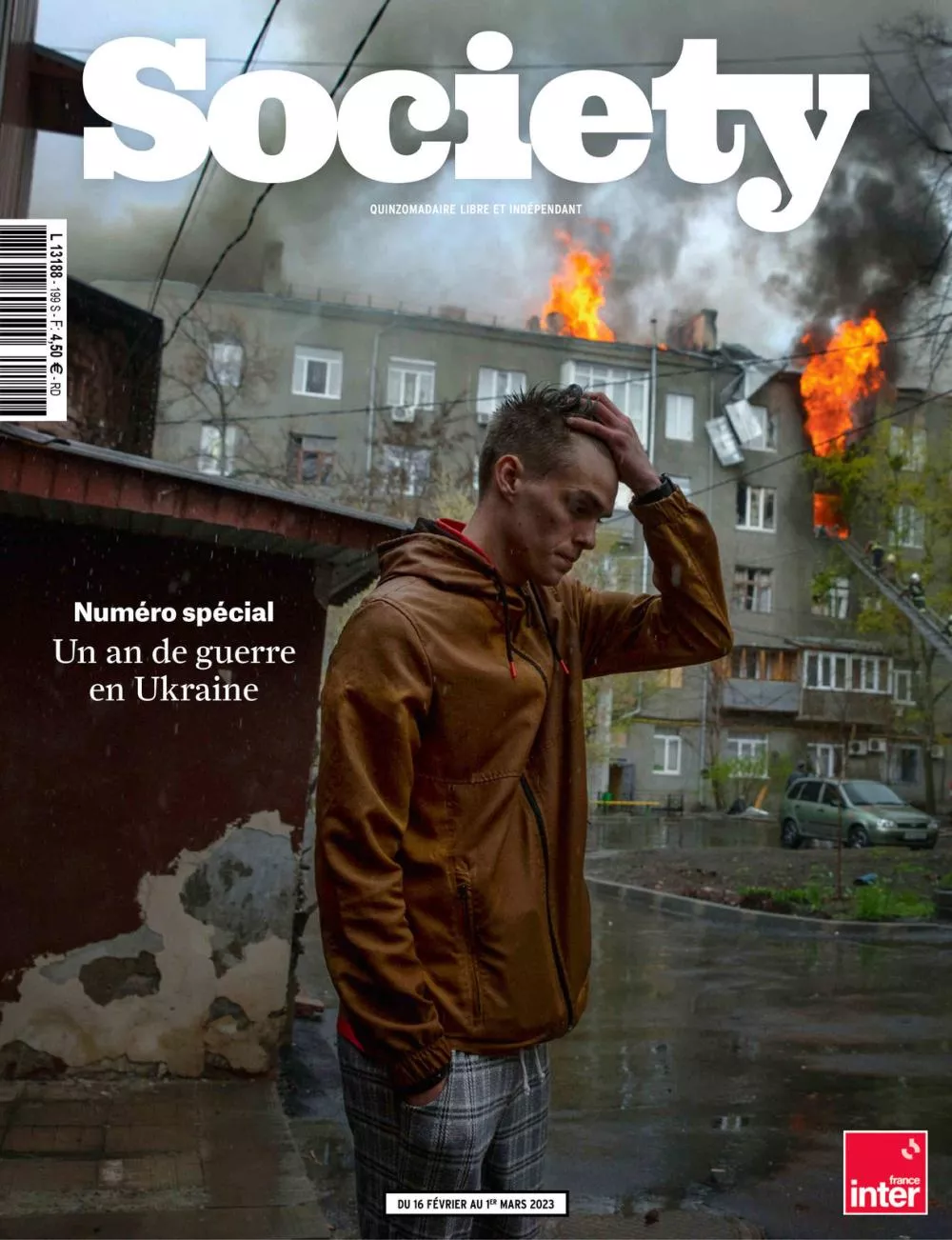 Un homme se tient devant un bâtiment en feu, avec des flammes et de la fumée s'élevant du toit. Il a l'air préoccupé, avec une main sur la tête. C'est la couverture d'un numéro spécial du magazine "Society" sur un an de guerre en Ukraine.