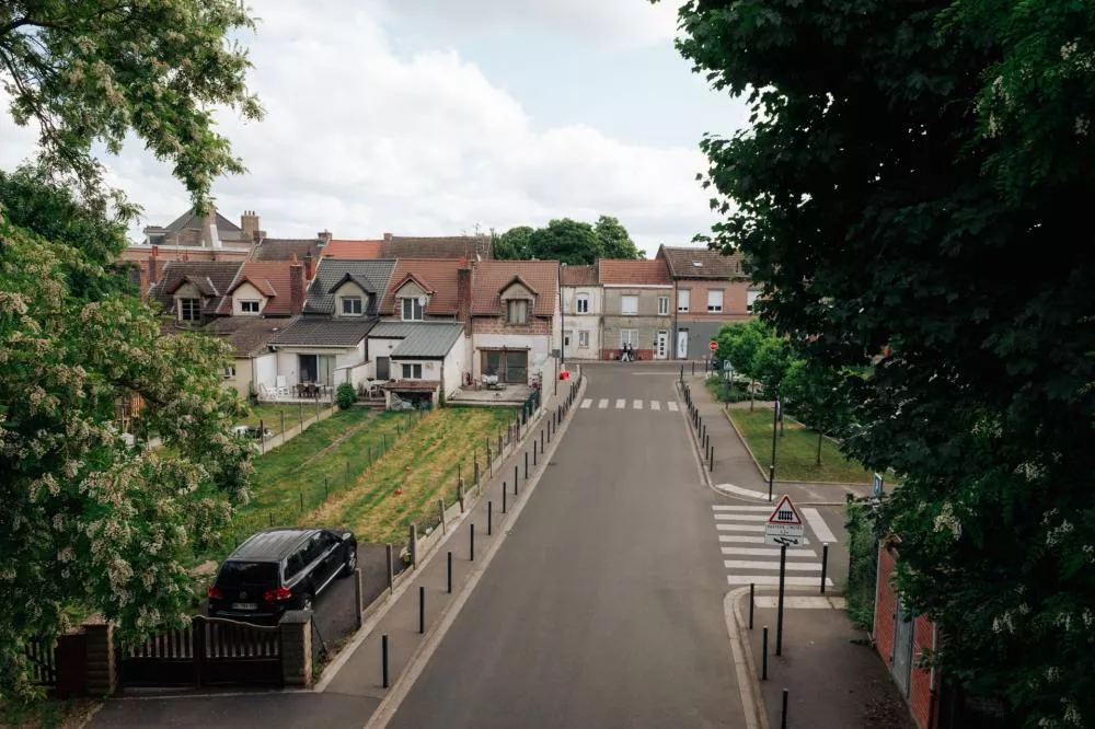 Une rue résidentielle avec des maisons alignées de chaque côté, une voiture garée à gauche et un passage piéton visible au fond.