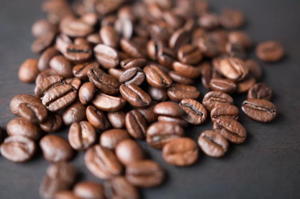Des grains de café bruns éparpillés sur une surface sombre.