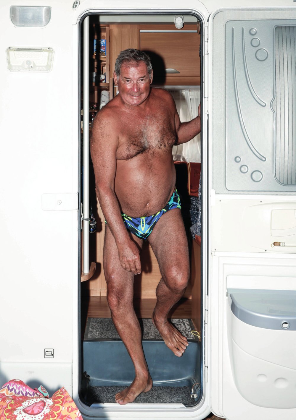 Un homme souriant en maillot de bain se tient dans l'entrée d'un camping-car.