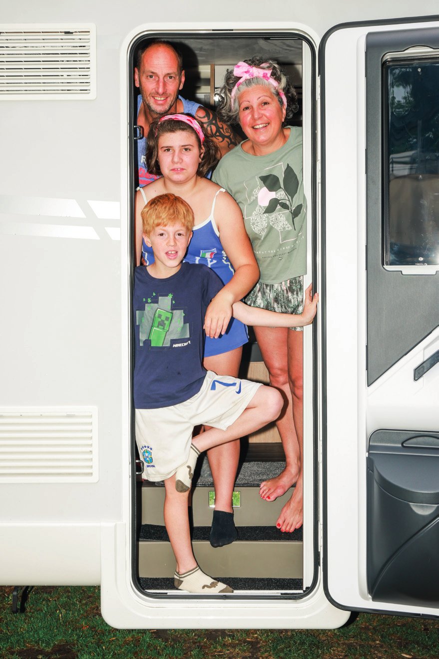 Une famille de quatre personnes se tient dans l'entrée d'une caravane. Ils sourient et semblent être en vacances ou en voyage.