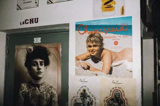 Un mur avec plusieurs affiches, dont une affiche colorée d'un événement nommé "Churrascaria" avec une personne allongée, et une affiche en noir et blanc d'une personne en tenue victorienne.