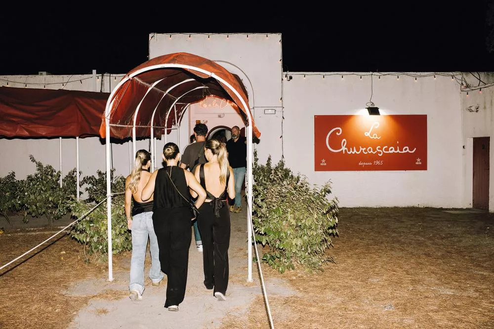Un groupe de personnes entre dans un restaurant nommé "La Churascaia" sous un auvent rouge.