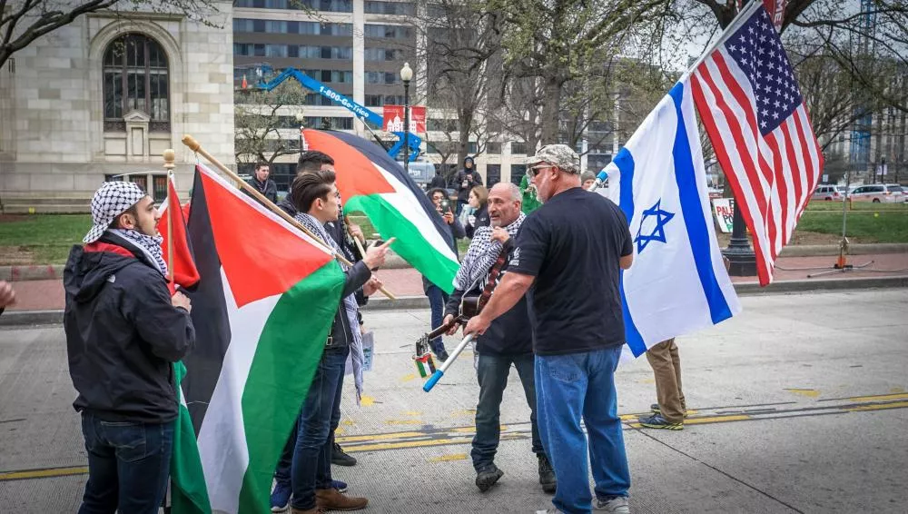 Des personnes tiennent des drapeaux palestiniens, israéliens et américains lors d'une manifestation ou d'un rassemblement.