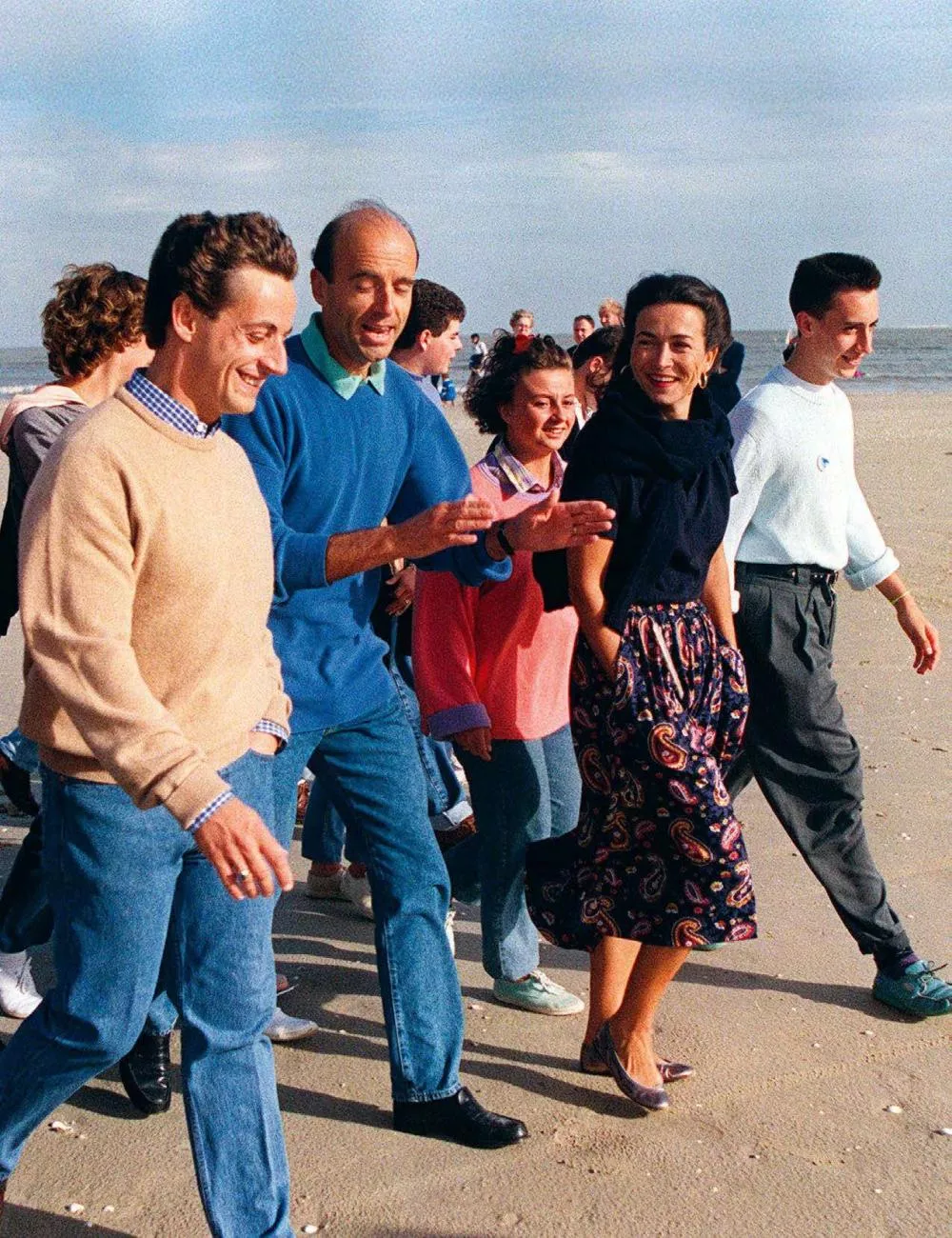Un groupe de personnes marchant ensemble sur une plage, discutant et souriant.