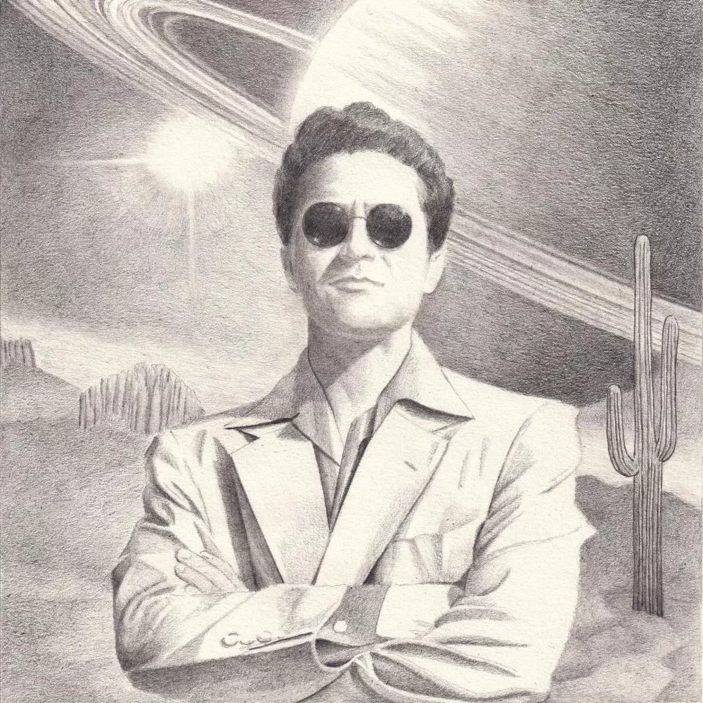 Un homme en costume avec des lunettes de soleil se tient les bras croisés devant un paysage désertique avec un cactus, sous un ciel où se dessinent des anneaux planétaires.