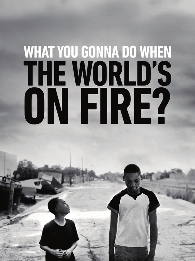 Deux personnes marchent sur un chemin pavé dans un environnement urbain en noir et blanc. Le texte dit : "What you gonna do when the world's on fire?"
