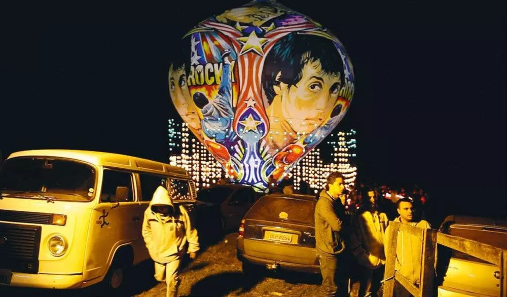 Un ballon coloré décoré de motifs et visages, entouré de personnes et de véhicules, illuminé dans la nuit.