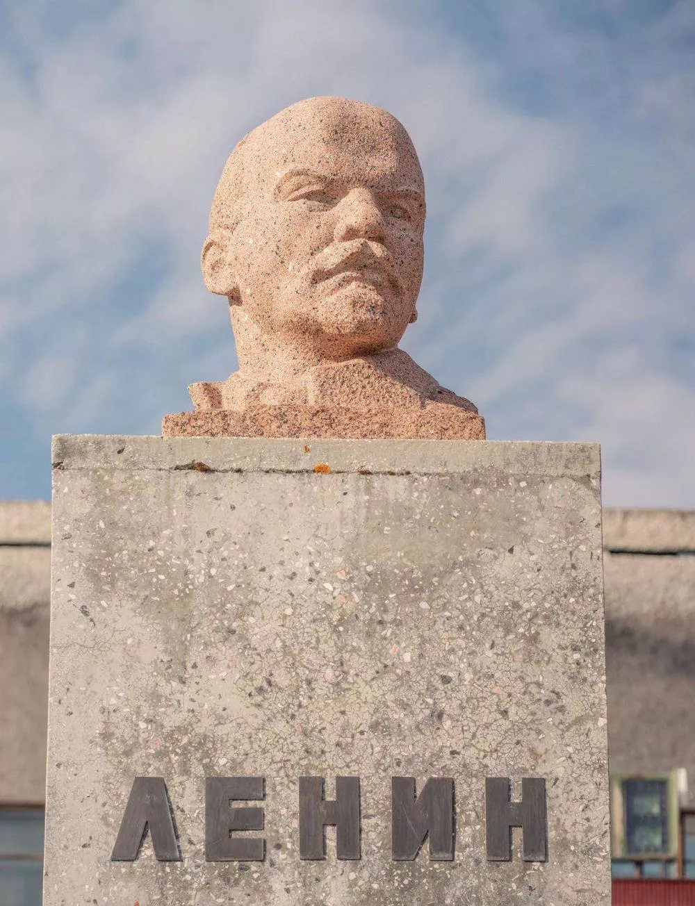 Un buste en pierre d'une personne est placé sur un socle en béton, avec le nom "ЛЕНИН" inscrit dessus.
