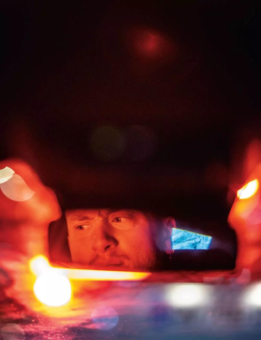 Un homme est visible dans un rétroviseur, avec des lumières rouges et bleues floues autour.