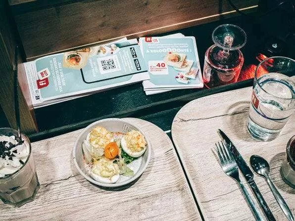 Un repas est servi sur une table avec un plat de salade, un verre d'eau, des couverts, et un milkshake avec de la crème fouettée. Des brochures sont posées à côté.