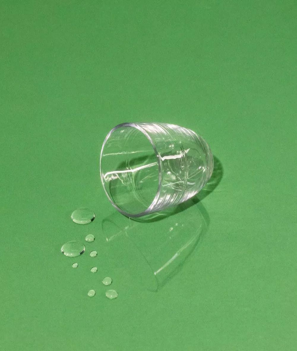 Un verre transparent renversé sur une surface verte avec quelques gouttes d'eau à côté.