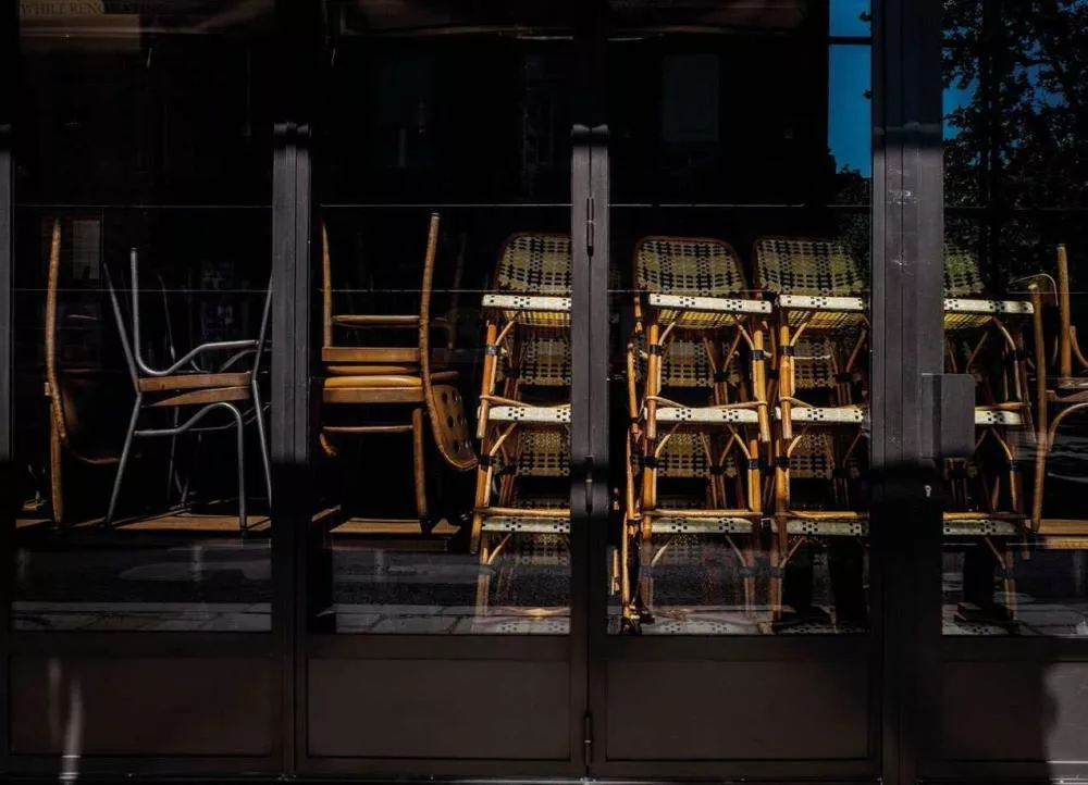 Un groupe de chaises empilées derrière une vitrine, avec des reflets sombres et une lumière contrastée.