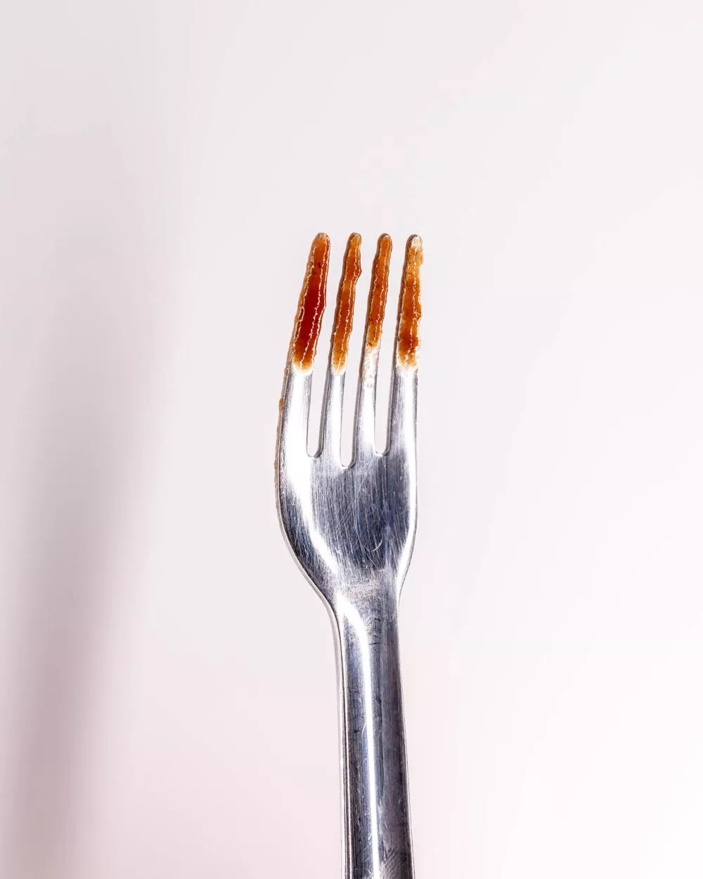 Une fourchette en métal avec de la sauce tomate sur les dents.