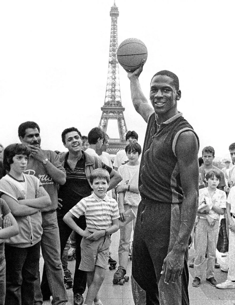 Un homme tenant un ballon de basket pose devant la Tour Eiffel, entouré de plusieurs personnes, dont des enfants.