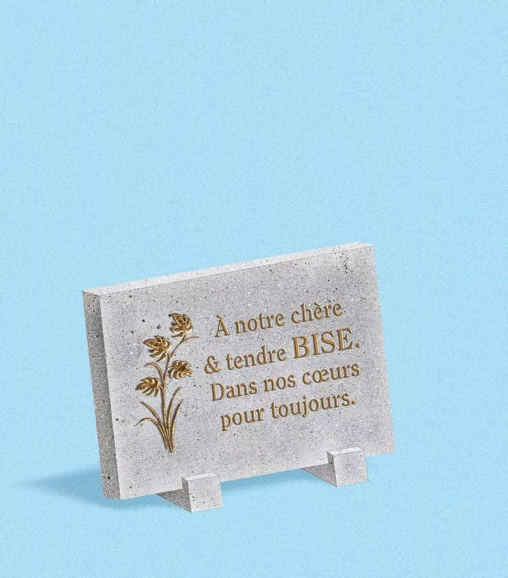 Une plaque commémorative avec un message en hommage à une personne chère, accompagné d'une décoration florale.