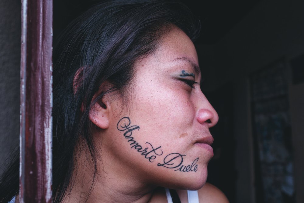 Une personne avec un tatouage sur la joue portant l'inscription "Amarte Duele".