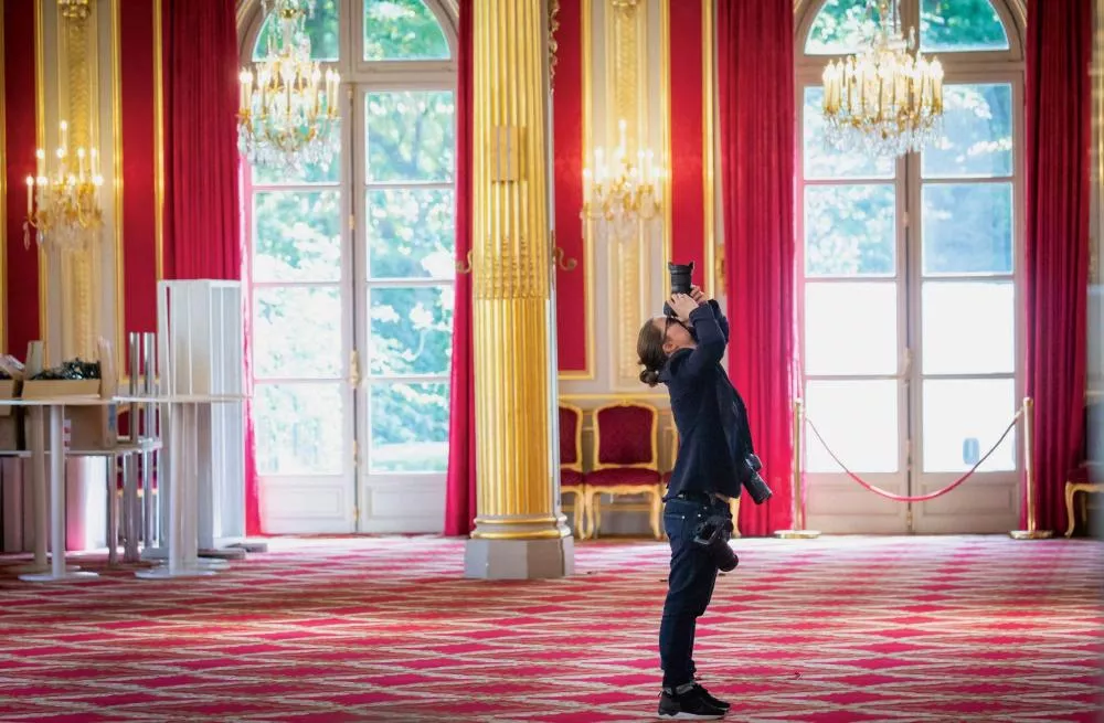 Une personne prend une photo à l'intérieur d'une salle élégante avec des colonnes dorées, des rideaux rouges et des lustres.