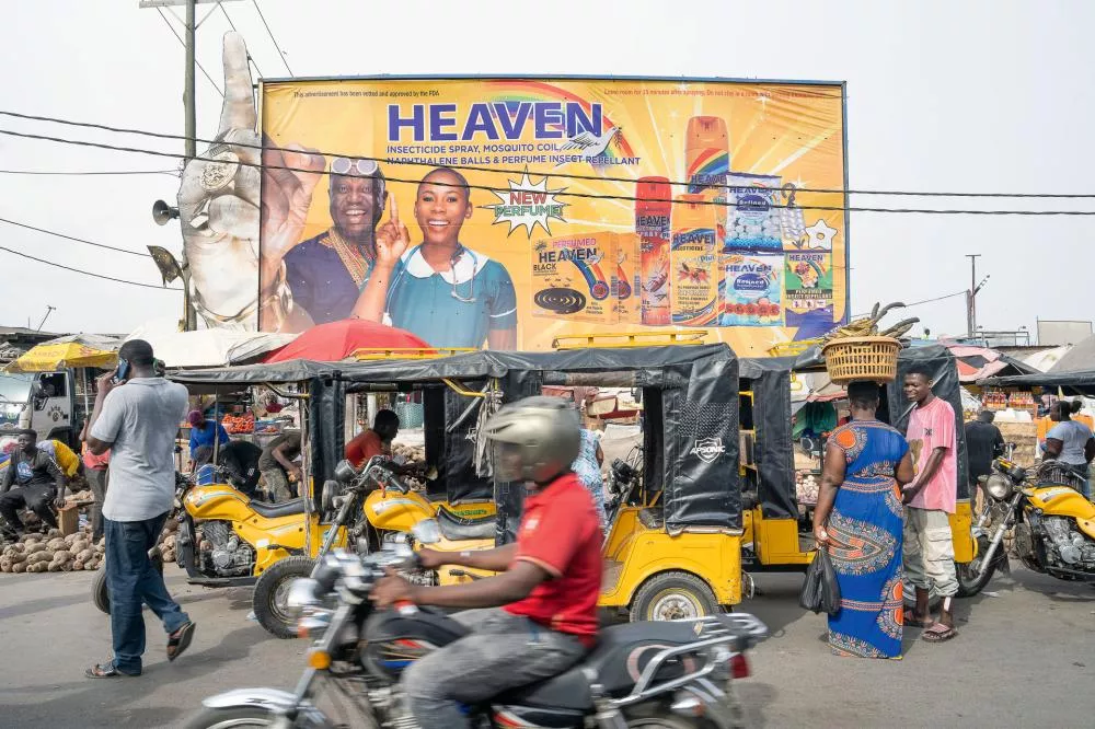 Une scène de rue animée avec des motos et des tuk-tuks jaunes, et en arrière-plan, un grand panneau publicitaire pour des produits insecticides de la marque "Heaven".
