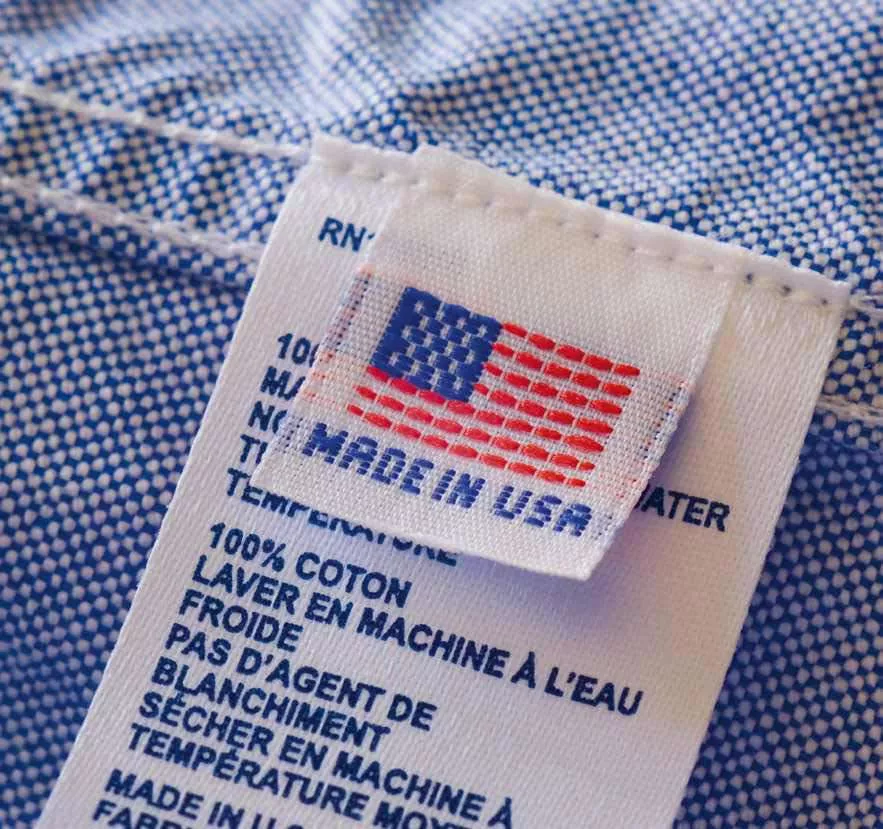 Étiquette de vêtement indiquant "Made in USA" avec des instructions de lavage en français, précisant que le tissu est 100% coton et doit être lavé à l'eau froide sans agent de blanchiment.