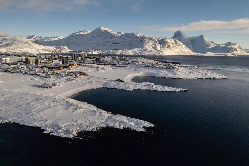 Une ville côtière enneigée entourée de montagnes, avec des bâtiments modernes et traditionnels, bordant une mer calme.