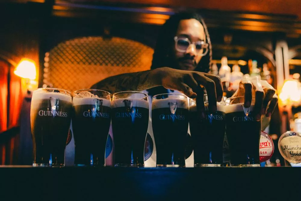 Un barman sert plusieurs pintes de Guinness dans un bar éclairé de manière chaleureuse.