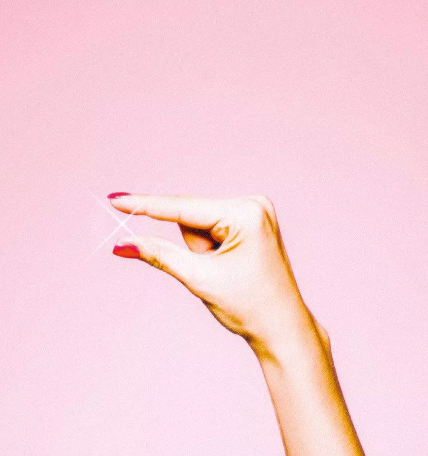 Une main avec des ongles peints en rouge tient quelque chose d'invisible entre le pouce et l'index, avec un effet d'étincelle lumineuse à l'endroit où les doigts se rejoignent, sur un fond rose.
