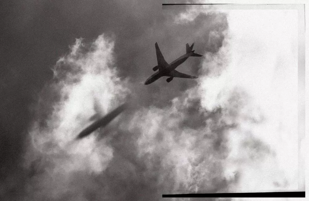 Un avion en vol au-dessus des nuages avec son ombre projetée sur les nuages. L'image est en noir et blanc.