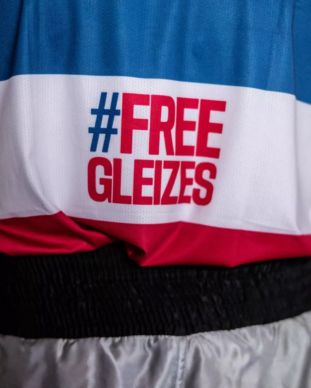 Un vêtement avec l'inscription "#FREE GLEIZES" en rouge et bleu sur fond blanc.