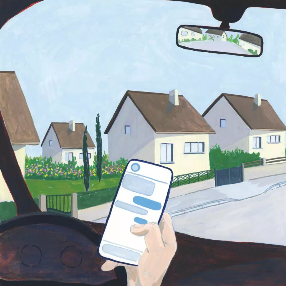 Une personne est dans une voiture, tenant un téléphone avec un écran de messagerie visible, et regarde des maisons de style résidentiel par la fenêtre.